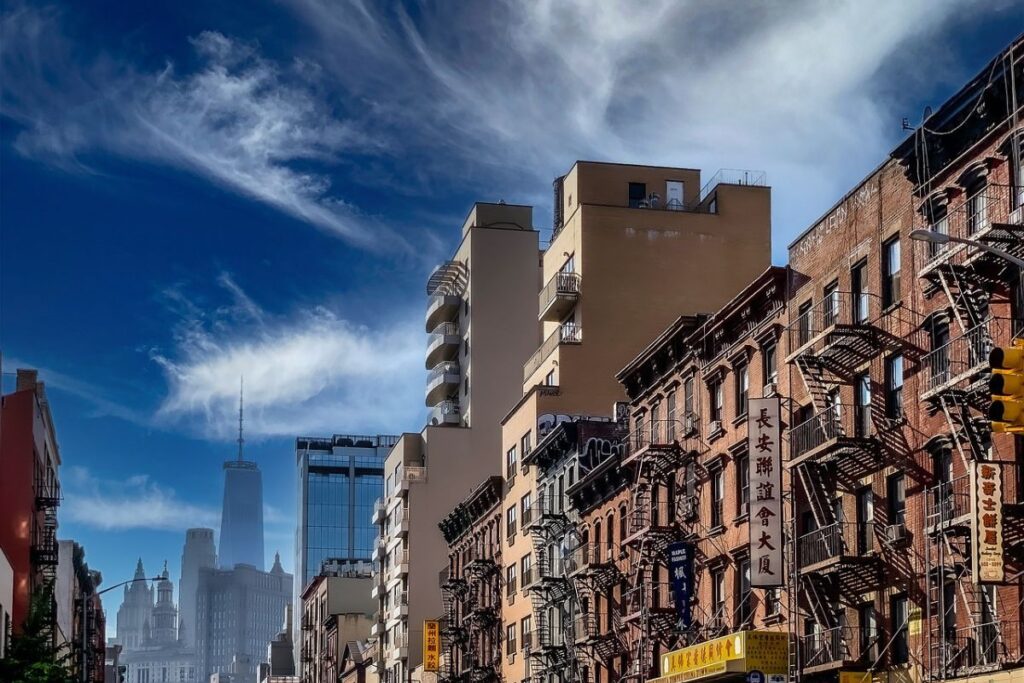 A  street in Chinatown, New York City, featuring historic brick buildings with fire escapes, Chinese signage, and modern skyscrapers in the background