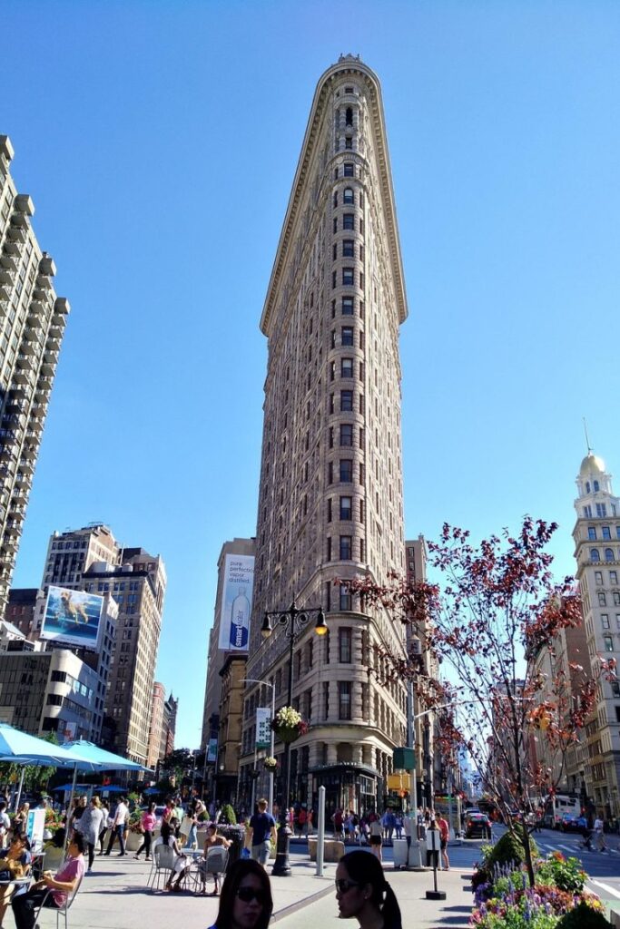 The Flatiron Building in New York City on a bright, sunny day, with lots of people strolling around