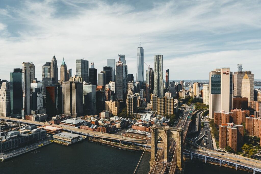 A scenic view of the New York City skyline with towering skyscrapers, including One World Trade Center, and the Brooklyn Bridge in the foreground