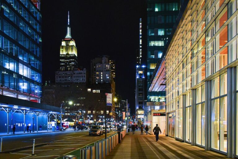 A nighttime view of a busy street in New York City, with the Empire State Building glowing in the background