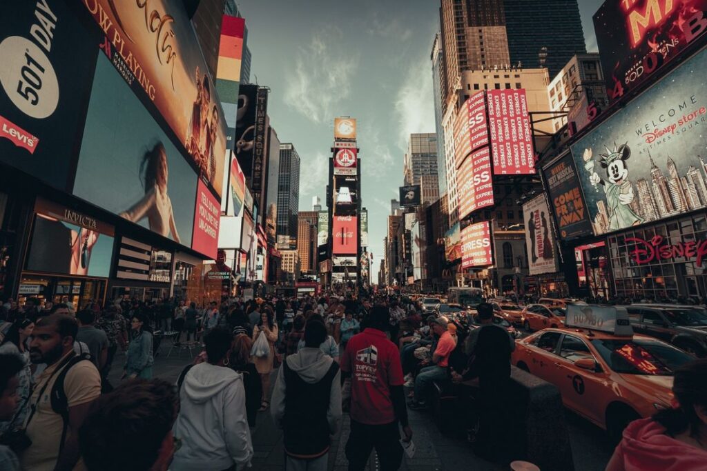 A busy scene in Times Square, New York City, with bright billboards, yellow taxis, and a crowd of people walking through the streets