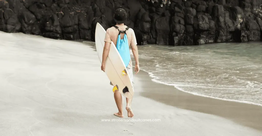Man walking along a peaceful Hawaiian beach with a surfboard—perfect for exploring Kihei’s calm beaches and surf-friendly shores.