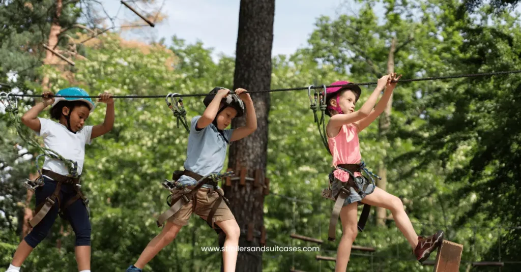 Three kids wearing helmets and harnesses crossing a zip line adventure course in a lush forest, ideal for outdoor fun.